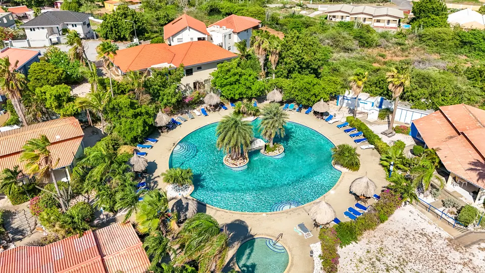 Dronefoto van het grote ronde zwembad van Seru Coral Resort met palmeneiland en palapa's