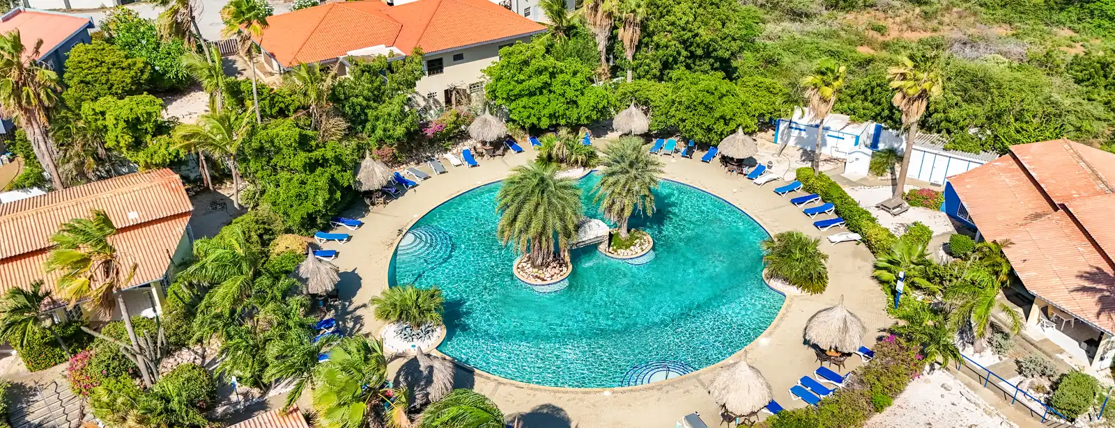 Dronefoto van het grote zwembad van Seru Coral Resort met palmeneiland en palapa's