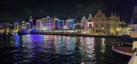De verlichte gevels van de Handelskade in Willemstad bij nacht, gespiegeld in het water