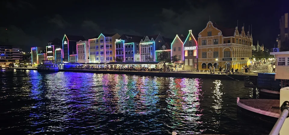 De verlichte gevels van de Handelskade in Willemstad bij nacht, gespiegeld in het water